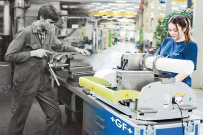 Half of the photo is in black and white and shows a male worker using simple machinery, the other half is a modern color image of a female around modern technology
