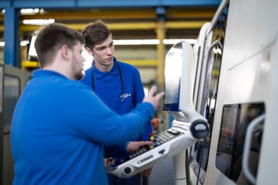 Two apprentices standing at a machine.