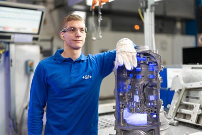 Apprentice standing beside a die-cast component, looking off into the distance