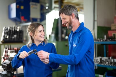 Trainer and apprentice look at each other, he shows her a measuring device.