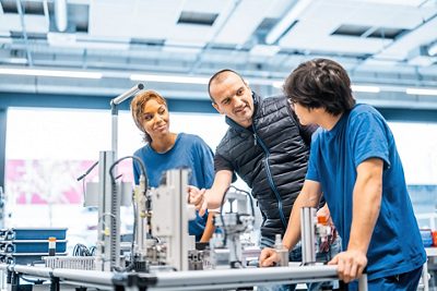 Ein Praxisbildner zeigt den Lernenden, wie man eine Maschine bedient.