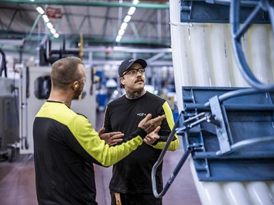 Two GF employees stand in a modern industrial facility, discussing the operation of a large machine.