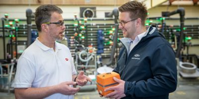 two men talking in front of system, one of them is carrying an electric actuator