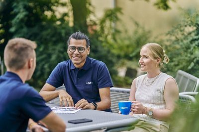 Three  GF colleagues sit together at an outdoor table, engaged in a friendly conversation.