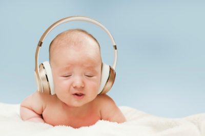 beautiful newborn baby in big headphones listening to music, isolated on blue background