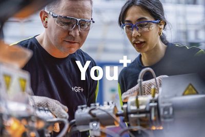 Two engineers work closely together on industrial machinery. They appear focused as they adjust components in a high-tech manufacturing environment. The text "You" is prominently displayed in the center of the image.